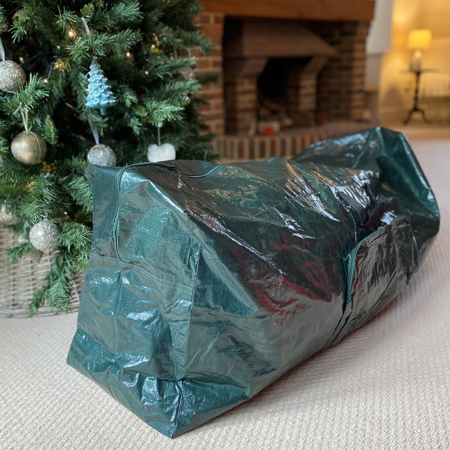A green Christmas tree storage bag with a Christmas tree and a fireplace in the background.