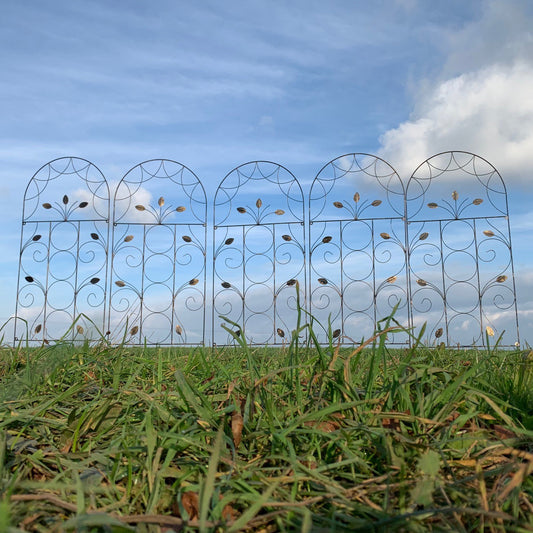 A set of five leaf design metal trellises placed on grass against a blue sky with clouds.