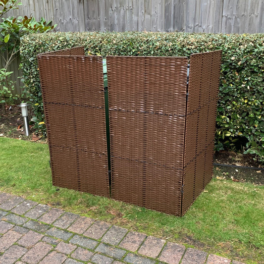 A brown rattan effect wheelie bin screen with double panels set against a hedge.