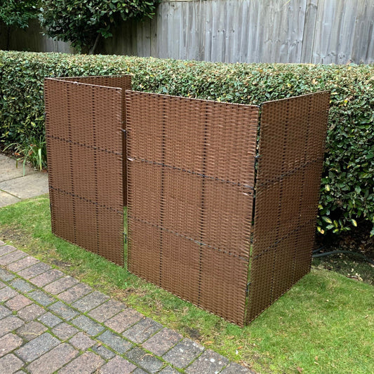 A rattan effect wheelie bin screen made of woven material over a metal frame, displayed in a garden setting.