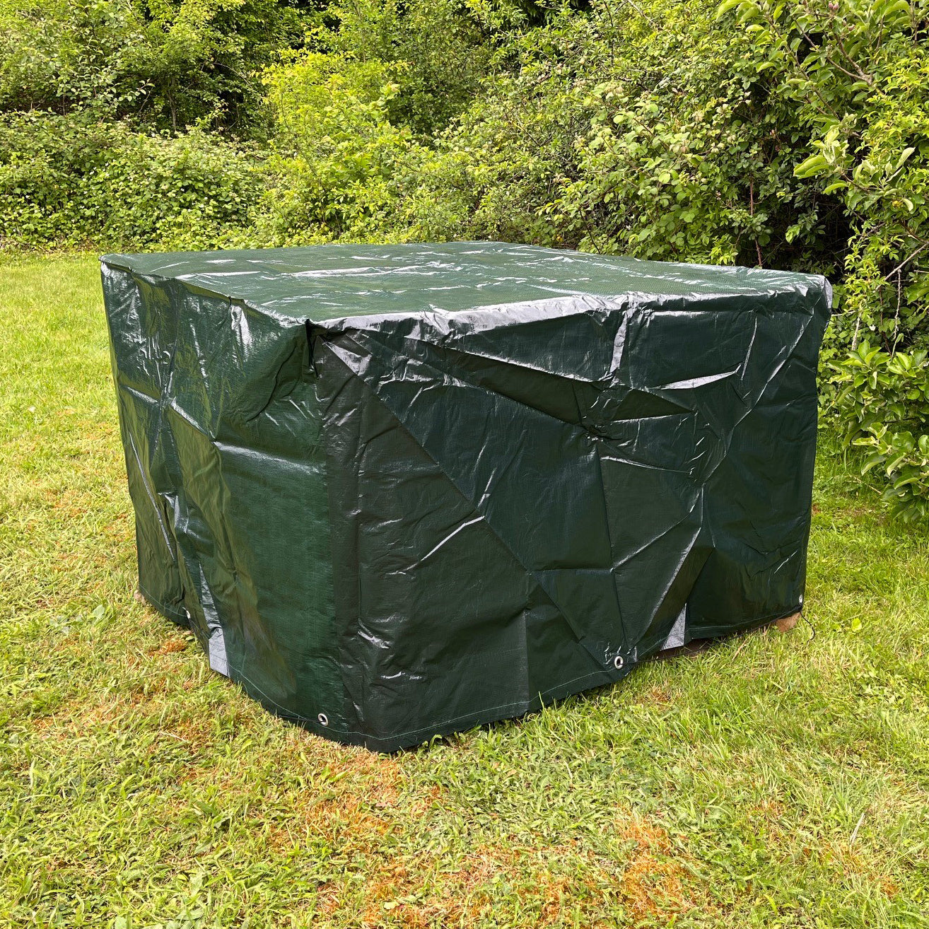 A green cube-shaped rattan garden furniture cover placed outdoors, presumably over a seating arrangement to protect it from elements.