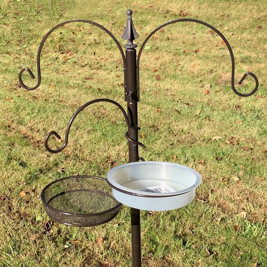 A metal bird feeding station with a mealworm tray and water dish, standing on grass.