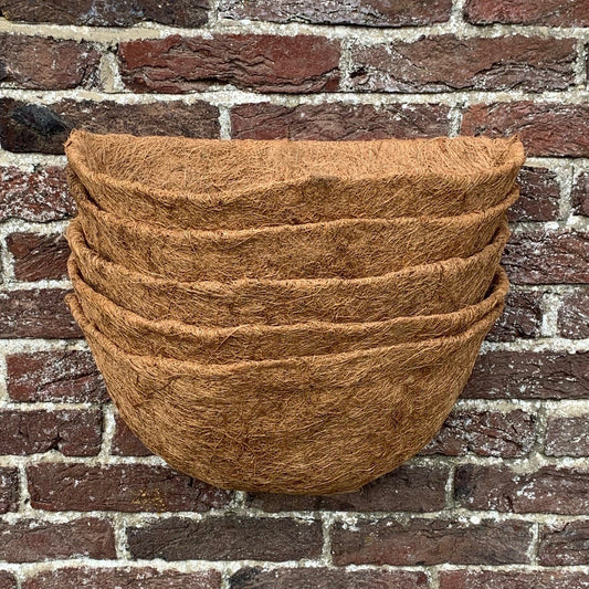 A stack of brown coco wall basket planter liners against a brick wall.