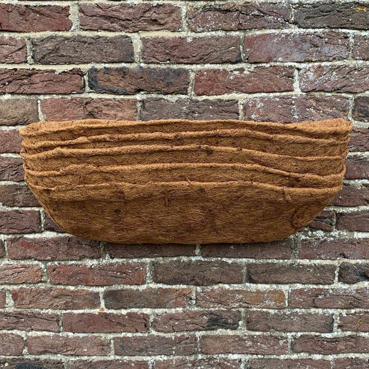 A brown coco fiber liner designed for use in a wall trough planter, displayed against a brick wall background.