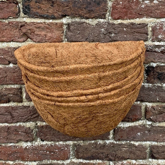 A stack of brown coco wall basket planter liners against a brick wall.