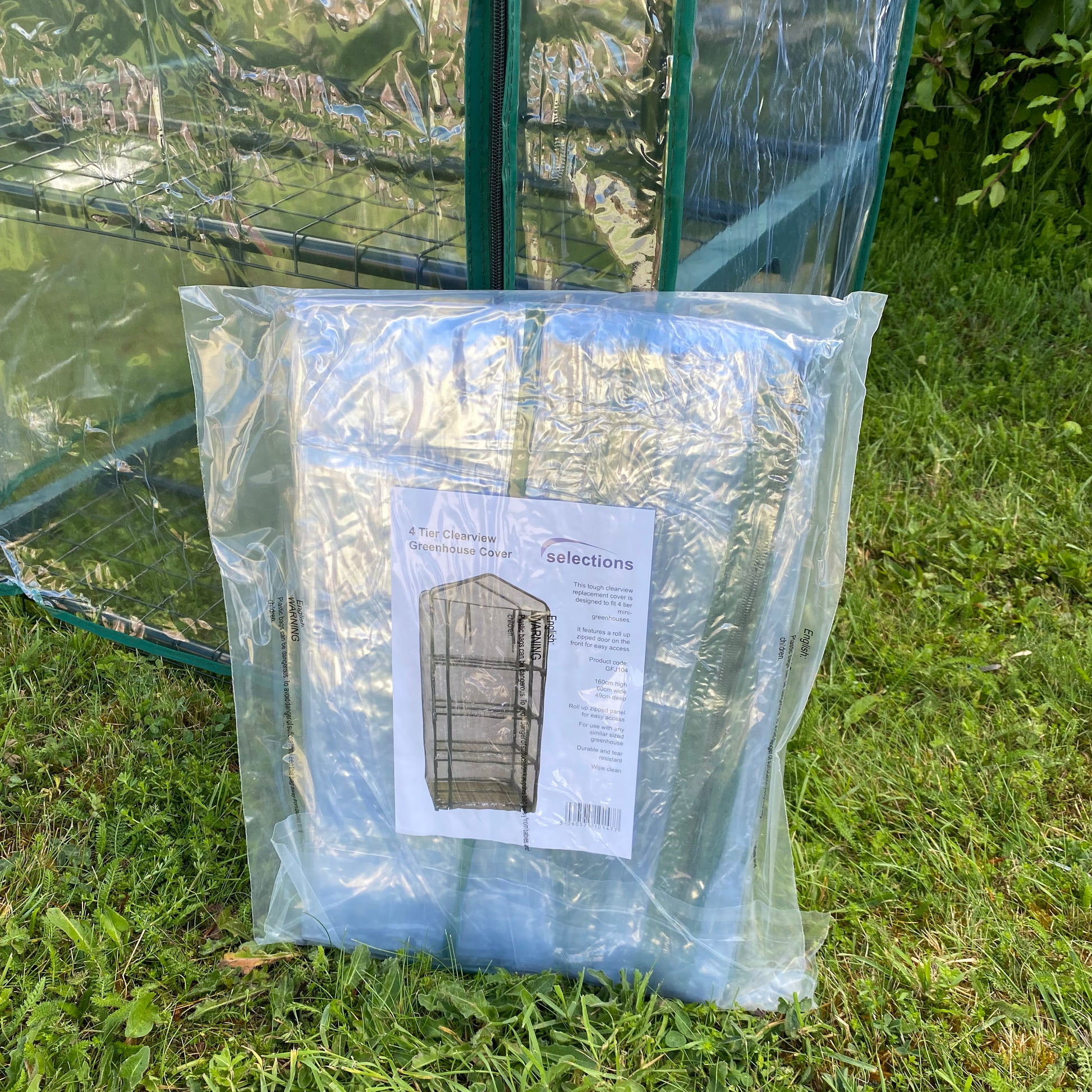 A packaged clear cover for a 4 tier mini greenhouse, displayed outdoors.