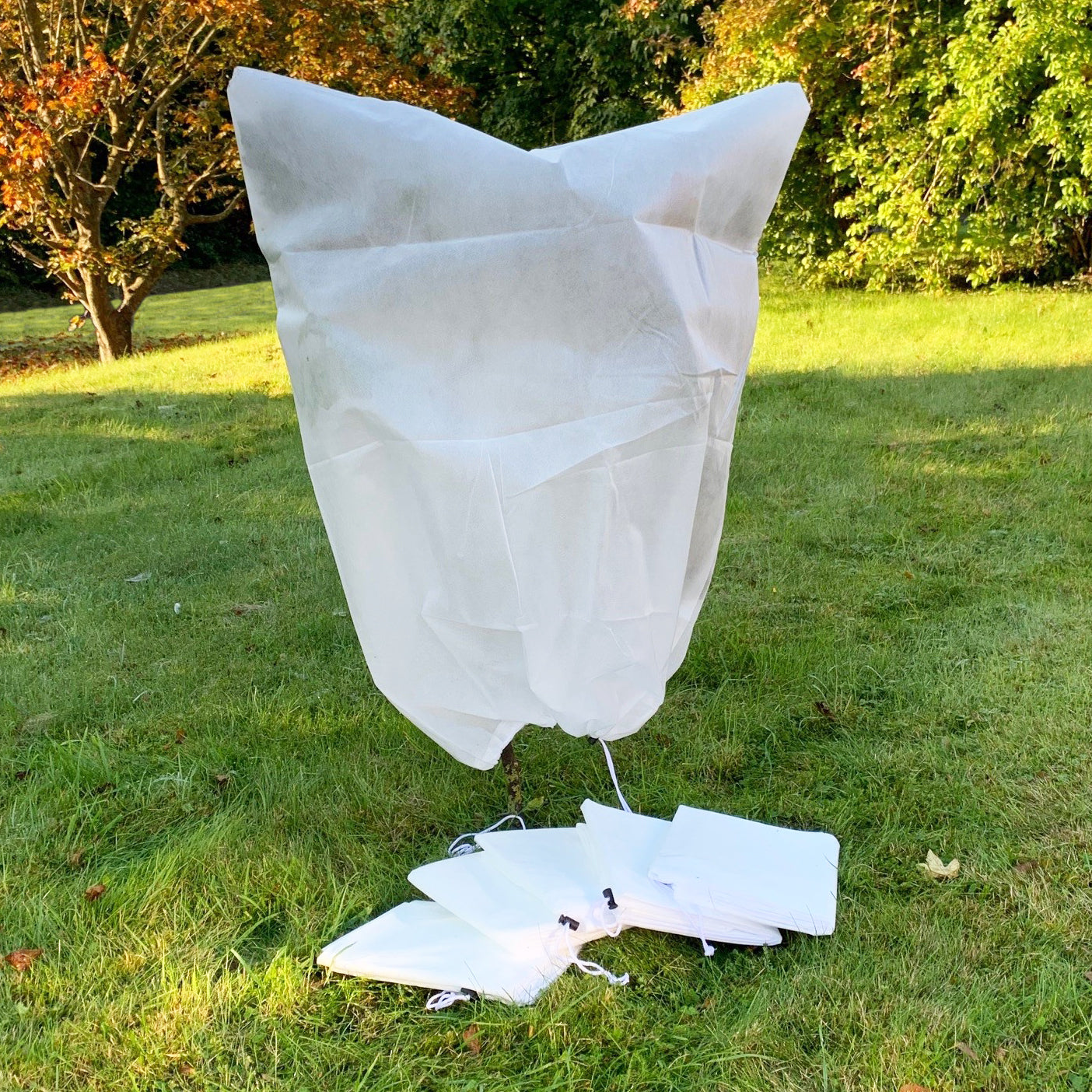 A white fleece plant protection jacket cover laid out on grass, appears to be empty or not fitted on a plant.