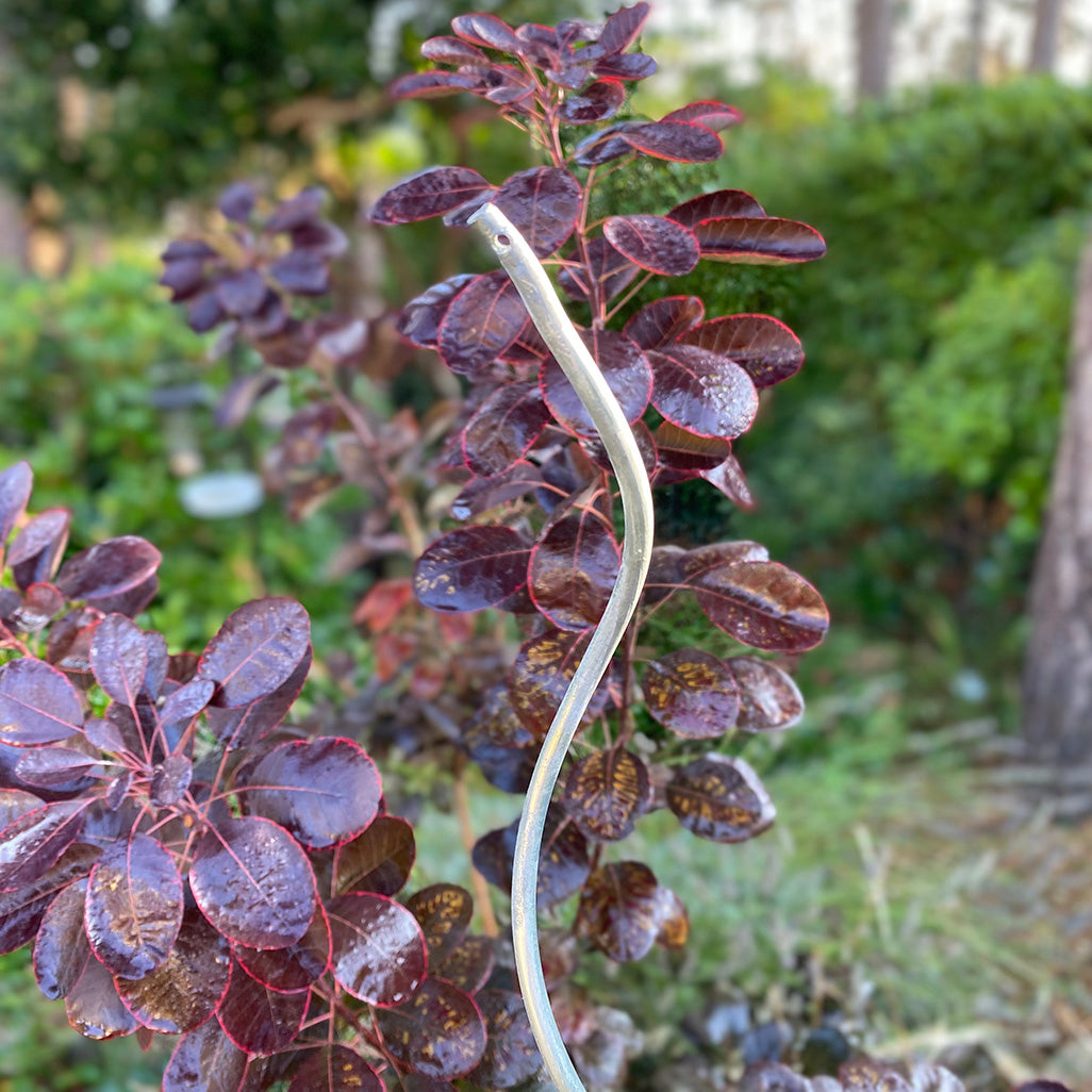 A galvanised metal plant support stake installed among purple foliage plants.