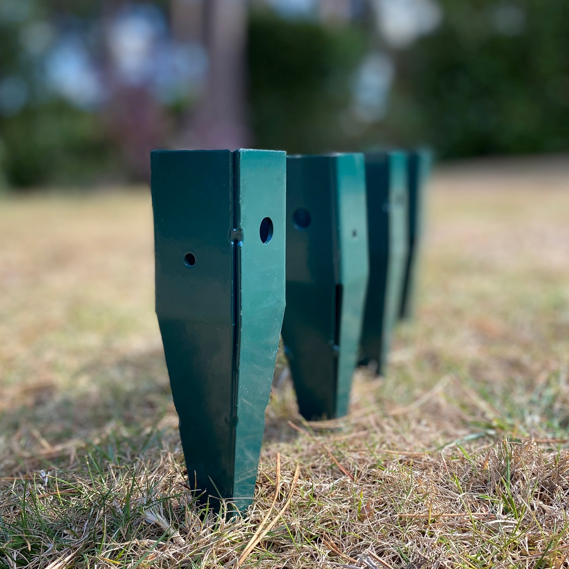 A set of four green painted steel ground spikes with screw holes, designed to be fixed into the ground to support a wooden garden arch.