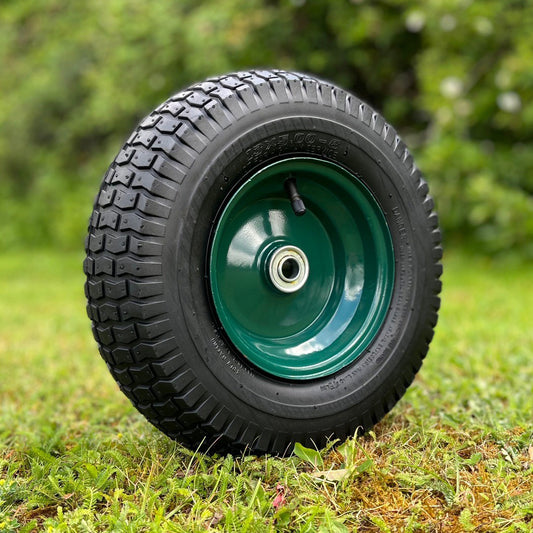 A black pneumatic replacement garden trolley wheel with a green metal rim, displayed on a grass background.
