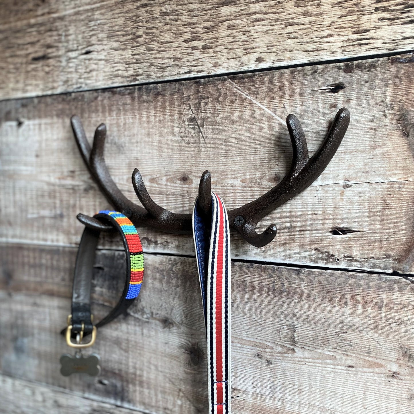 A wall-mounted cast iron coat rack with an antler design, featuring hooks for hanging items, mounted on a wooden wall.