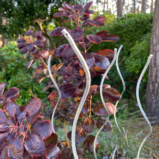 A set of silver-colored galvanised metal stakes installed in the ground, with a purple-leaved plant in the foreground.