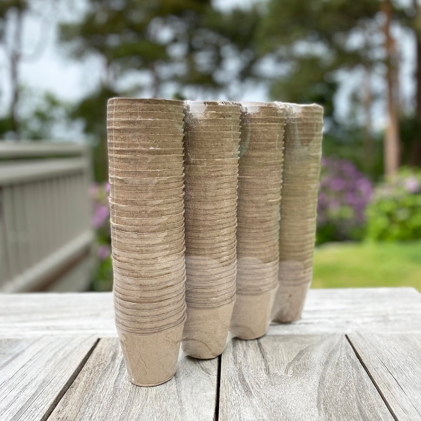 Stack of round, beige fibre plant pots on a wooden surface with a garden background.