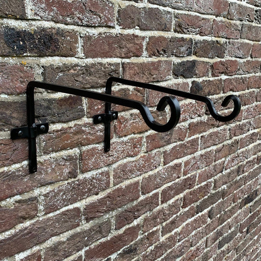 Black metal square hanging basket bracket mounted on a brick wall.