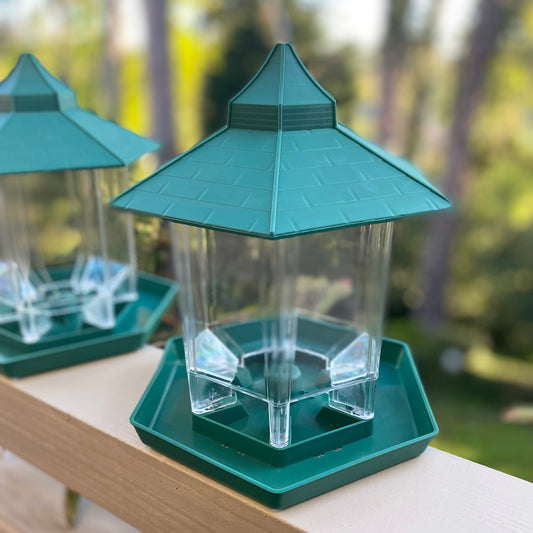 A set of two green bird feeders with a capacity of 600 grams each, hanging from a wire and placed on a wooden platform.