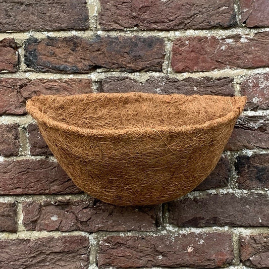 A brown coco wall basket planter liner placed against a brick wall.
