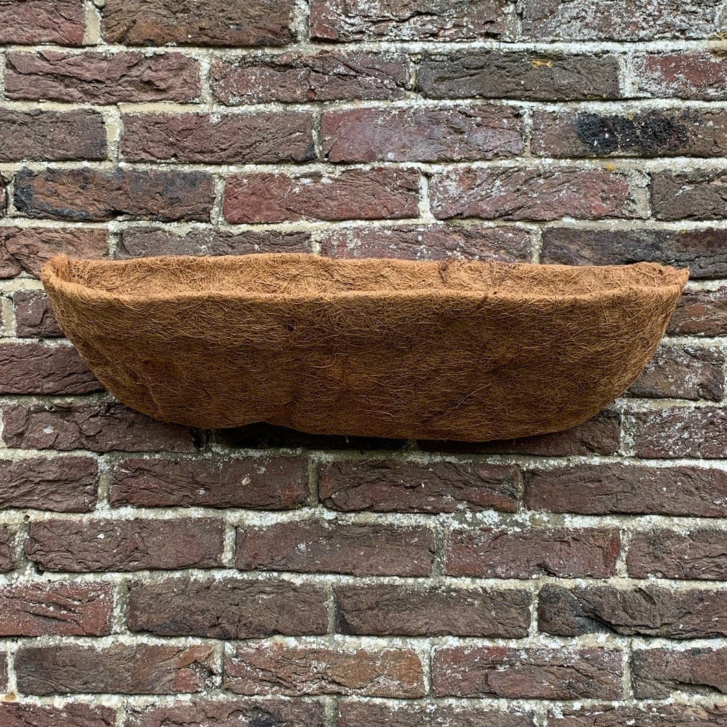 A brown coco wall trough planter liner placed against a brick wall.