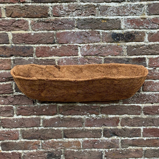 A brown Coco Wall Trough Planter Liner placed against a brick wall.