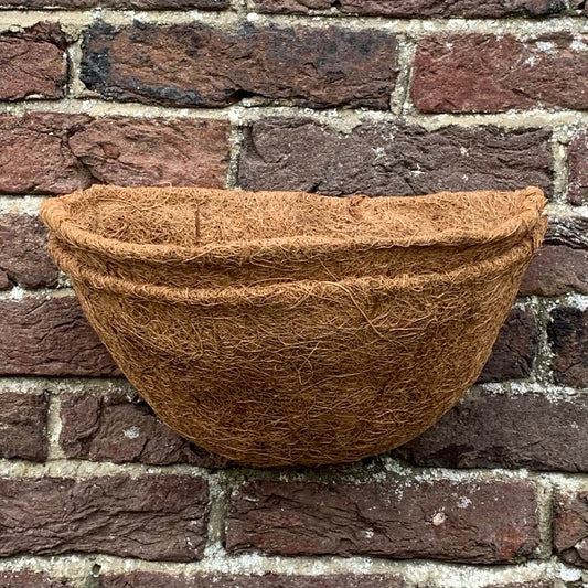 A brown coco wall basket planter liner placed against a brick wall.