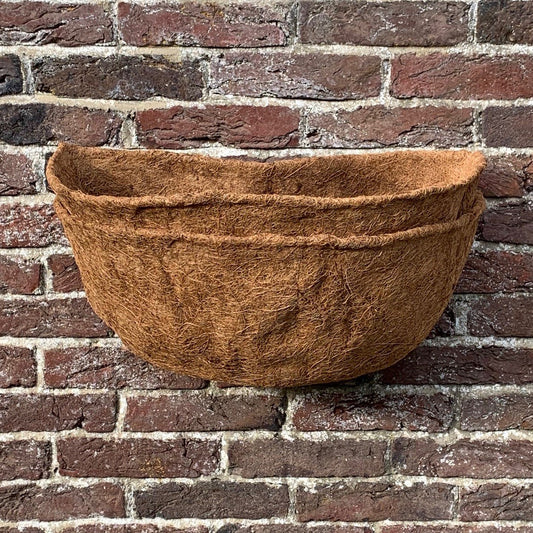 A brown coco wall basket planter liner placed against a brick wall.