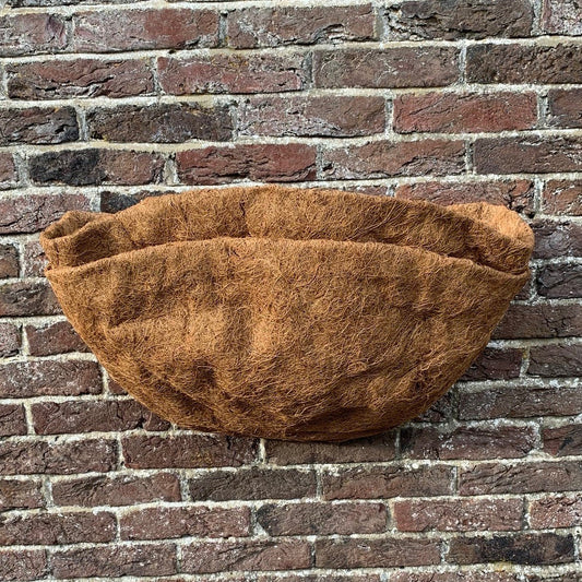 A brown coco wall basket planter liner displayed against a brick wall background.