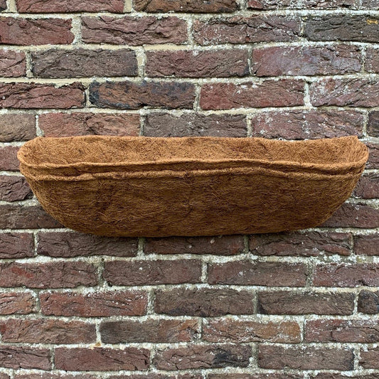 A brown Coco wall trough planter liner placed against a brick wall.