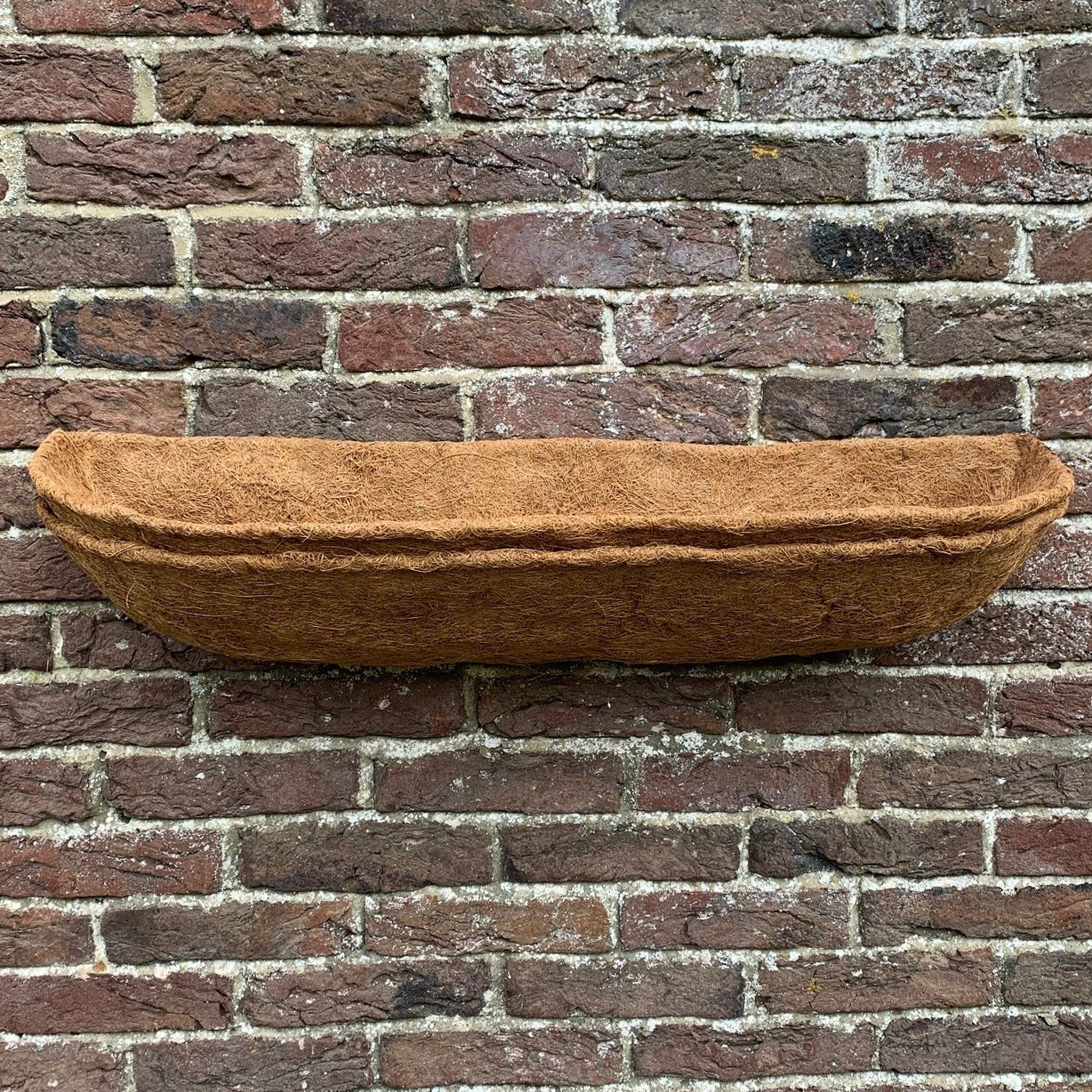 A brown coco wall planter liner placed against a brick wall.