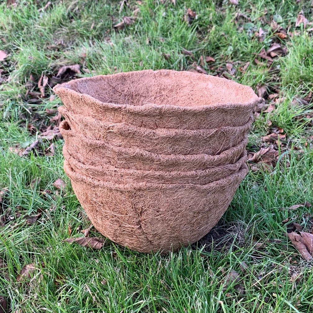 A stack of brown coir hanging basket planters on a grassy background.