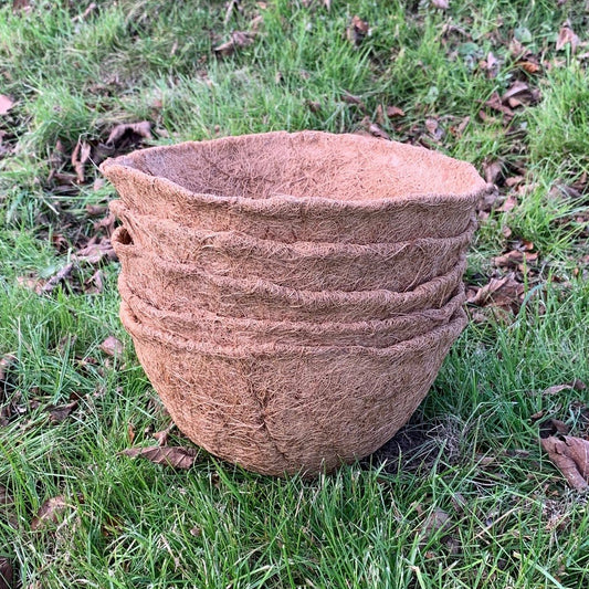 A stack of brown coir hanging basket planters on a grassy background.