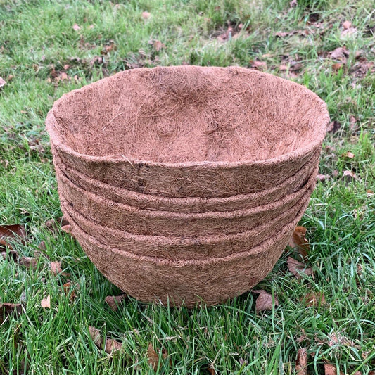 A stack of brown, round coco hanging basket planter liners on grass.