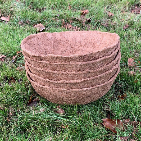 A stack of five round brown coco hanging basket planter liners on grass.