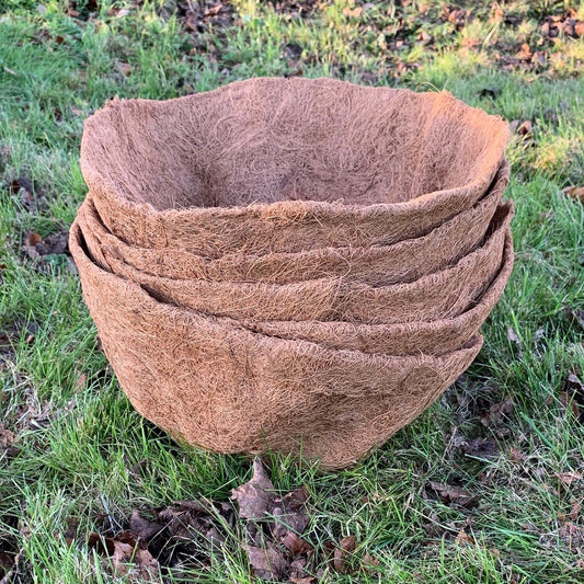 A stack of brown, round coco hanging basket planter liners placed on grass.