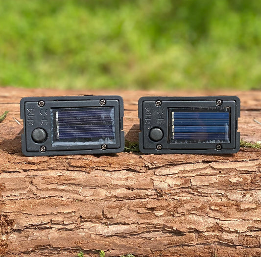 Two black solar-powered LED light boxes placed on a wooden surface, with solar panels on top.