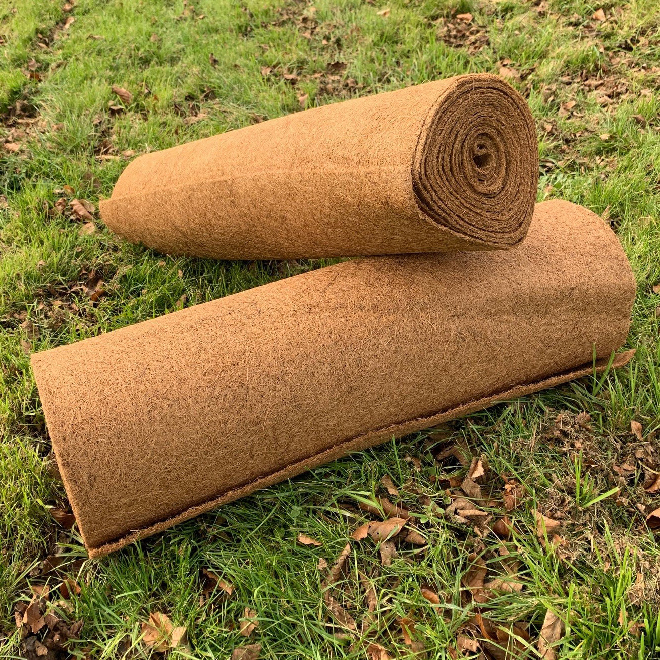 Two rolls of brown coconut fibre planter liners lying on a grass surface.