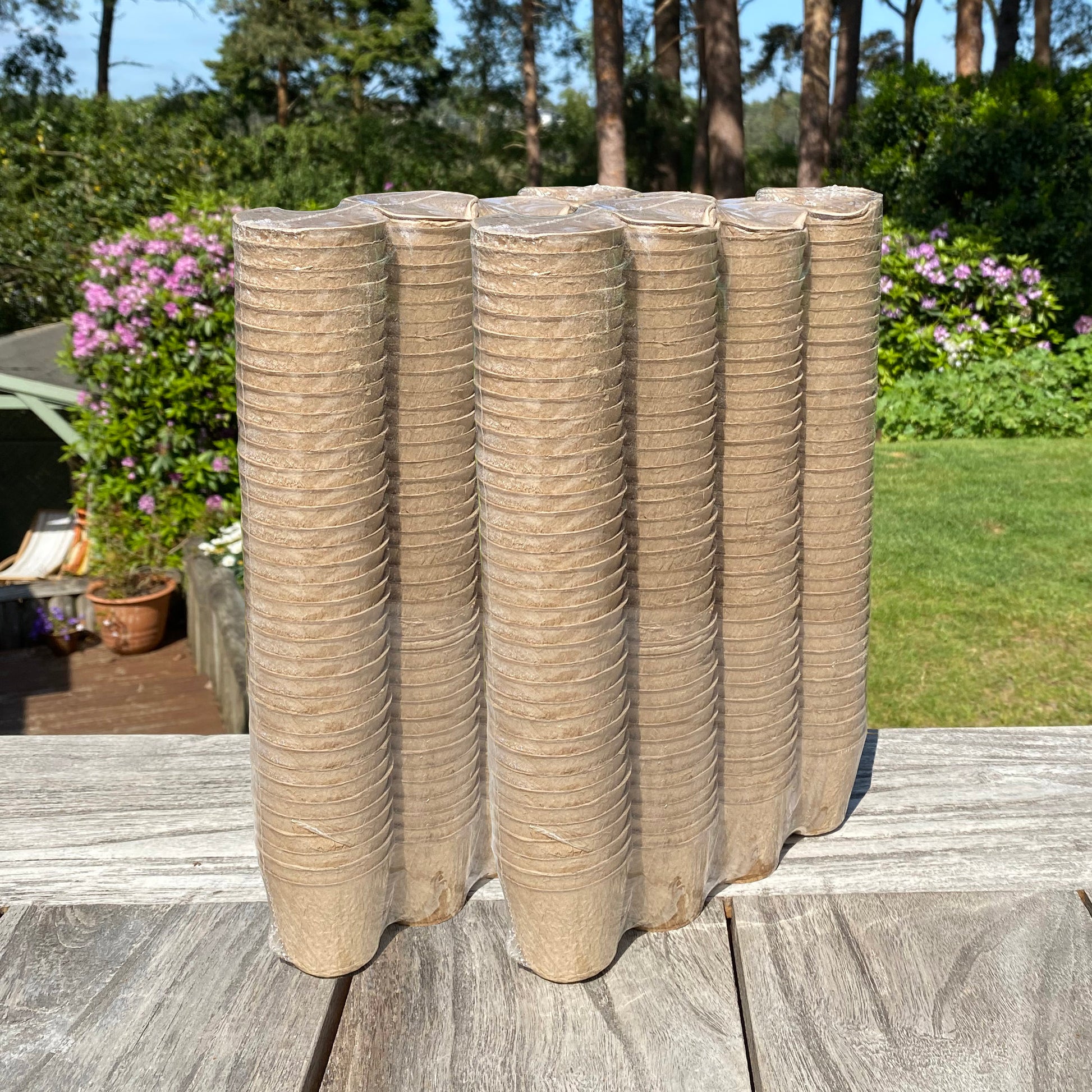 Stacks of round, beige fibre plant pots on a wooden surface with a garden in the background.