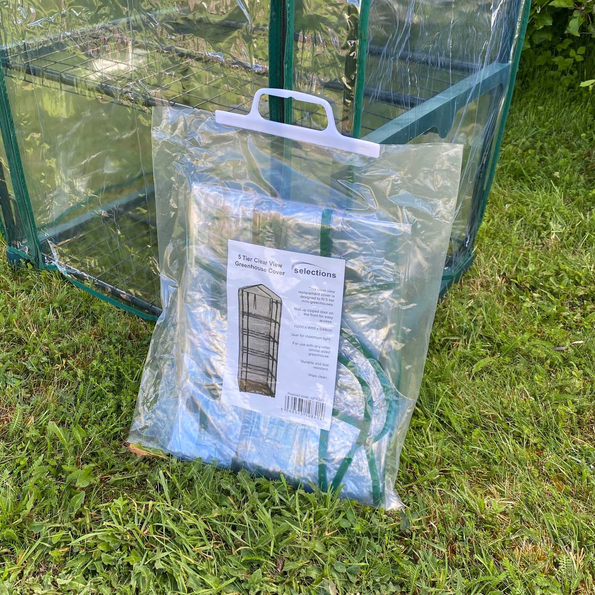 A clear plastic replacement cover for a 5 tier mini greenhouse, packaged and displayed on grass.