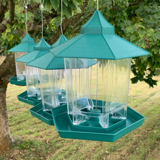 A set of four green bird feeders with clear plastic containers, hanging from wires.