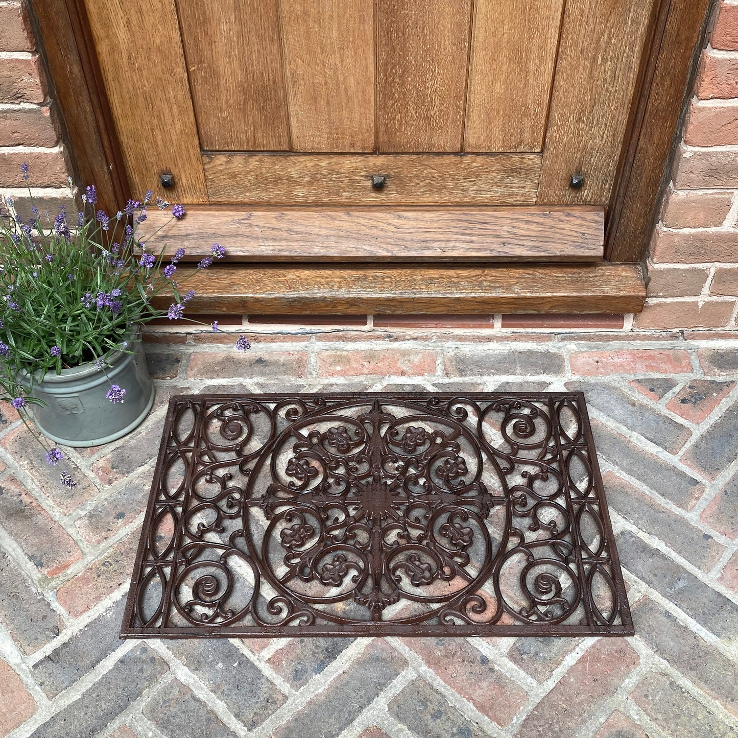 An ornate cast iron doormat with a rustic brown finish, placed on a doorstep.