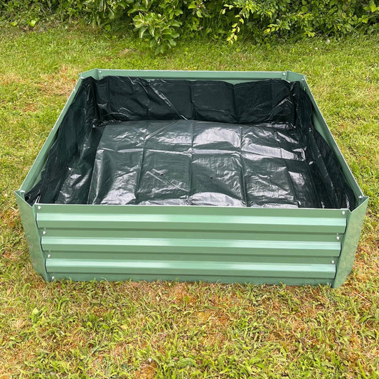 A black liner for a metal raised vegetable bed, placed inside the green bed which is set on a grass surface.
