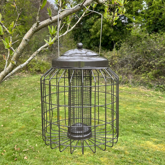 A black, heavy duty squirrel proof hanging bird nut feeder with a gun metal grey lid, displayed against a natural background.