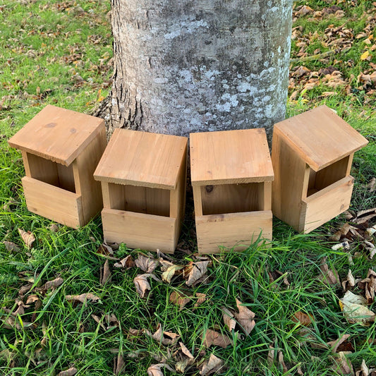 Four wooden Robin birdhouse nest boxes placed against a tree trunk in a garden setting.