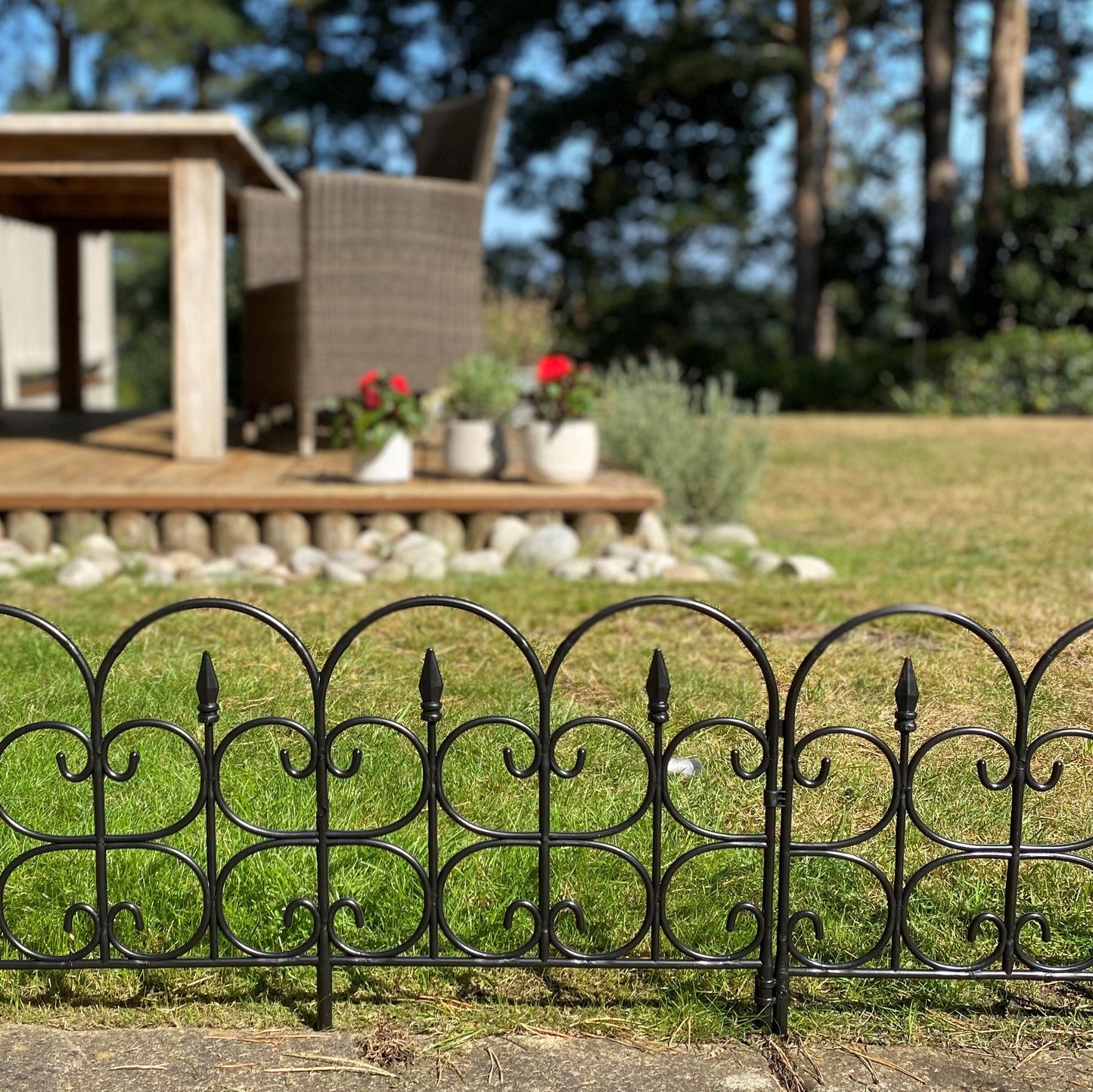Black plastic ornamental lawn edging panels arranged on grass forming a curved boundary. Background includes a wooden gazebo and garden.