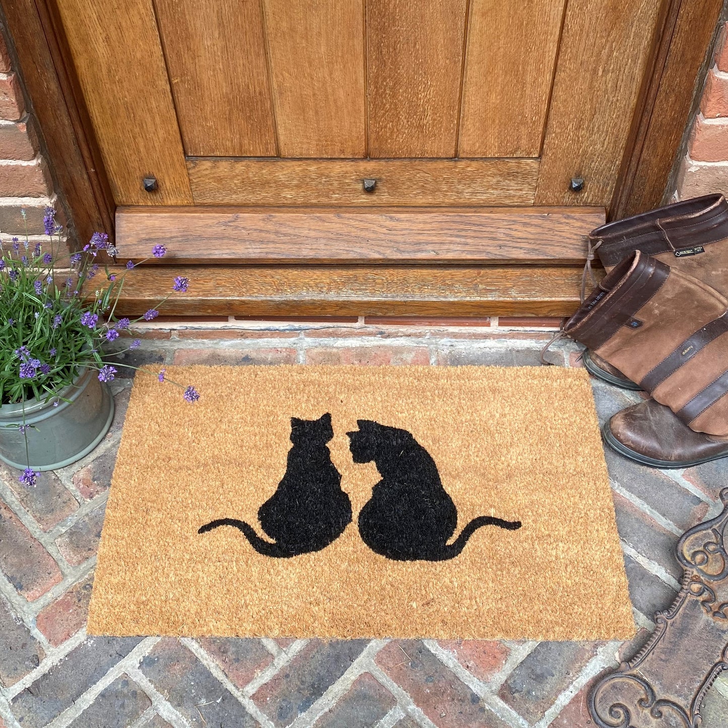 A coir doormat with an silhouette of two cats printed on it, placed on a doorstep.