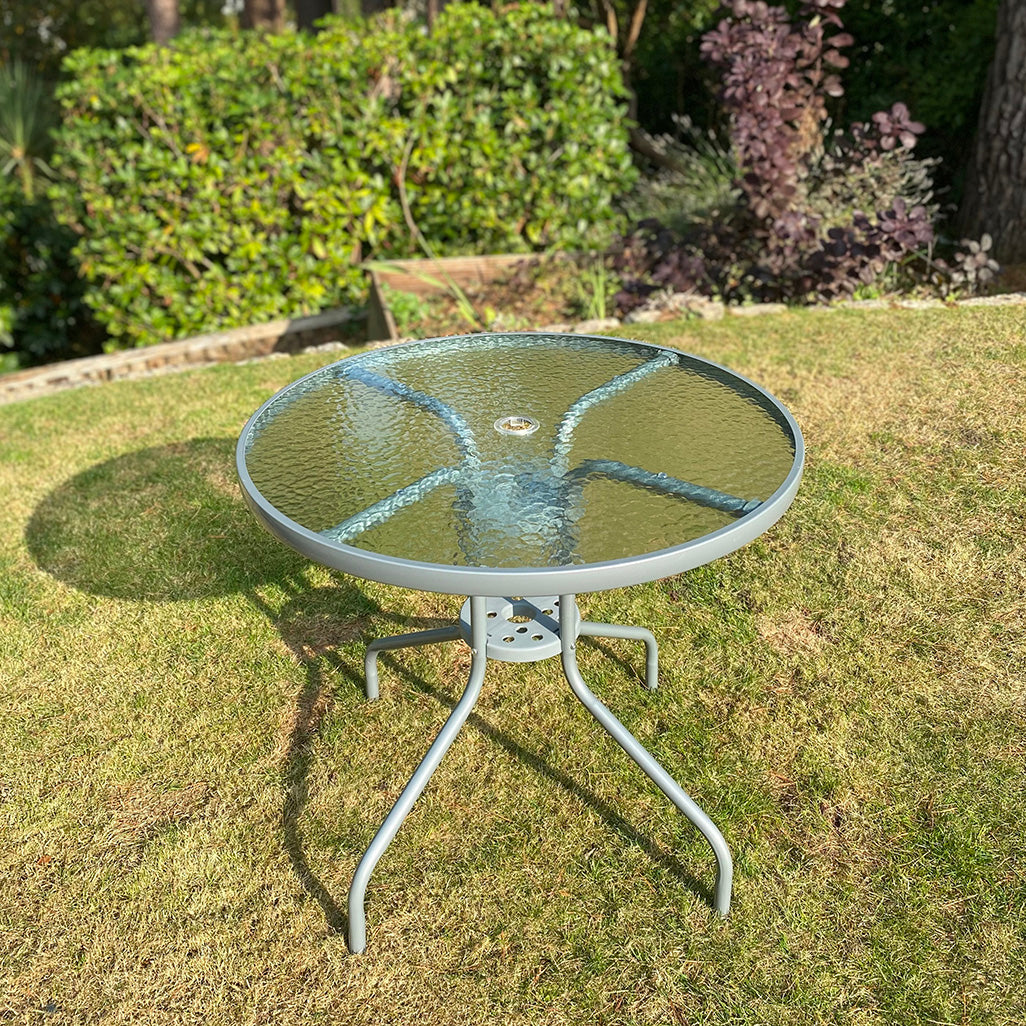 A round glass topped garden table with a metal frame, displayed on grass.