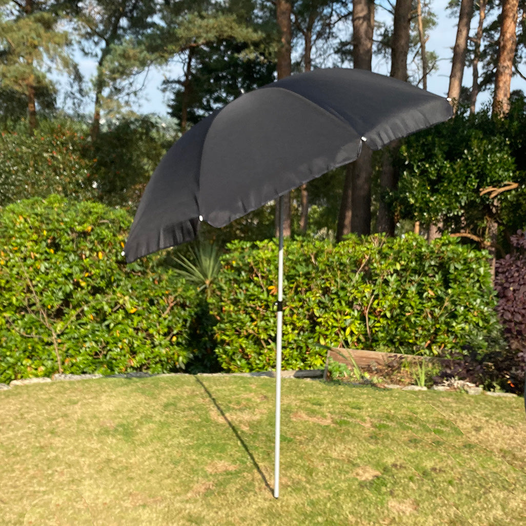 A black parasol with a metal pole, set on a grassy area, providing shade to garden furniture.