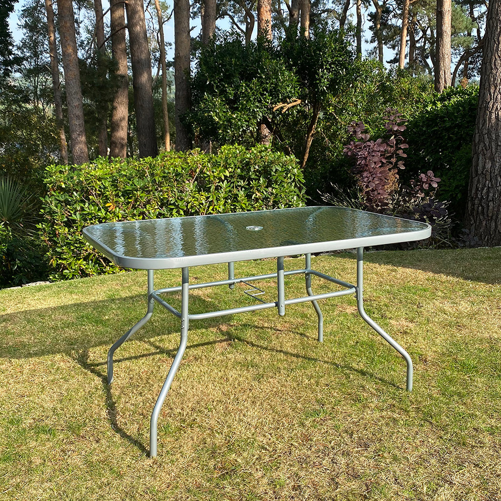 Rectangular garden table with a glass top and steel frame, displayed on a lawn.