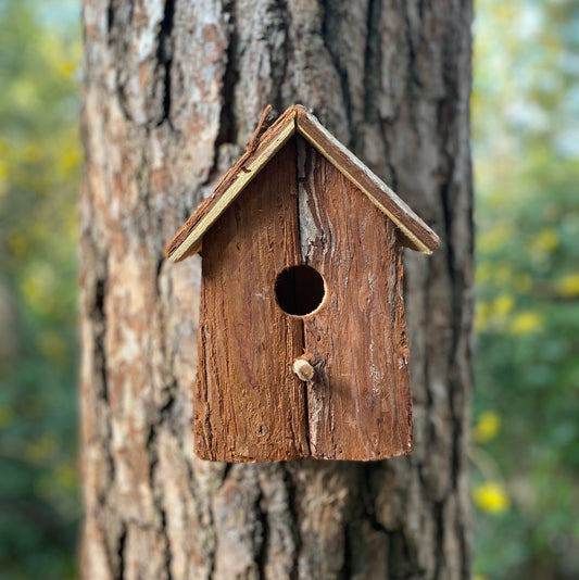 A rustic barkwood birdhouse nest box hanging on a tree trunk.