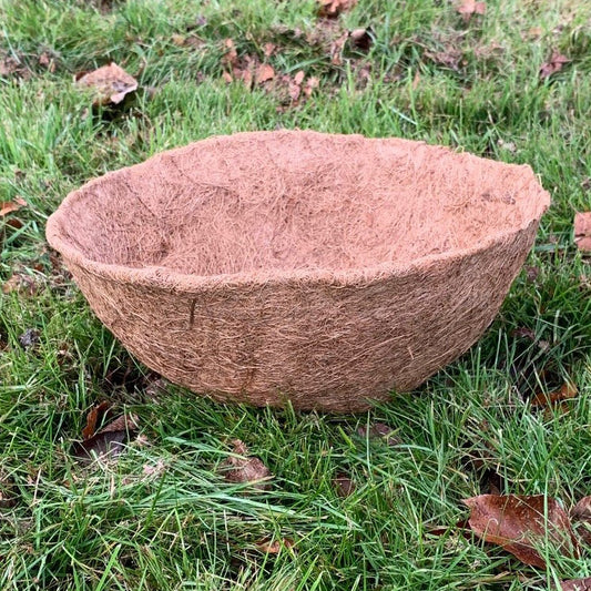 A brown coco hanging basket planter liner placed on grass.