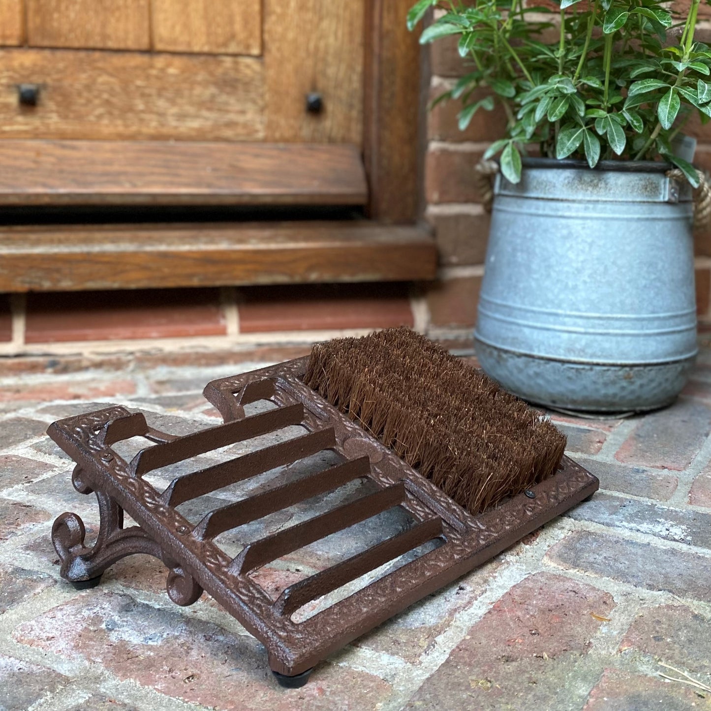 A traditional cast iron boot scraper and shoe brush with a vintage style design, placed on a doorstep.