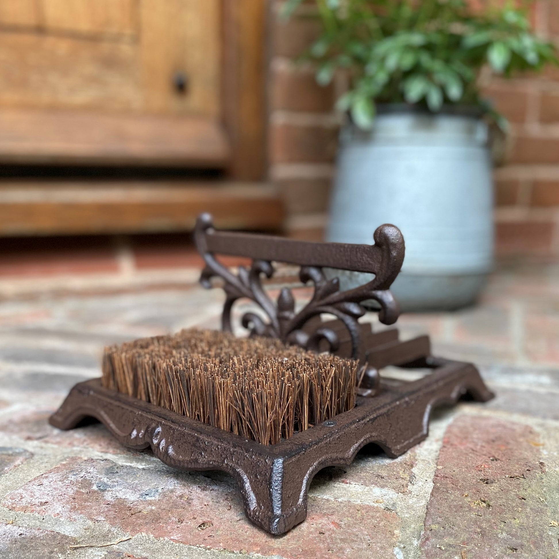 A traditional cast iron boot scraper and brush with ornate Victorian vintage style decoration, placed on a brick surface.